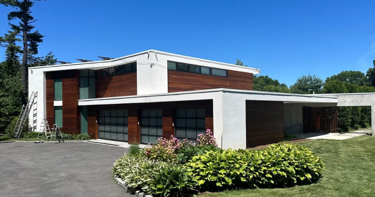 Finished modern home exterior with white stucco, warm wood siding, and black-framed windows.