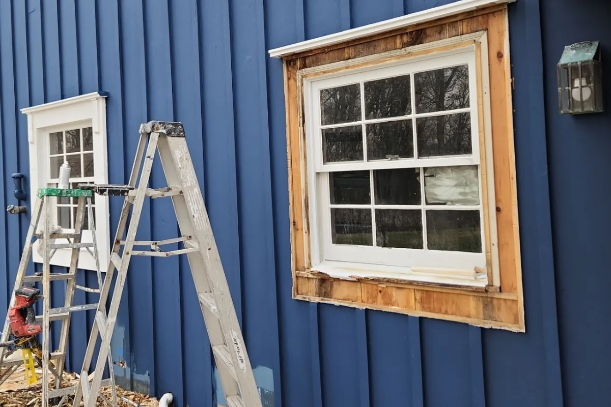 Peeling paint on wood siding above a garage before scraping and sanding.