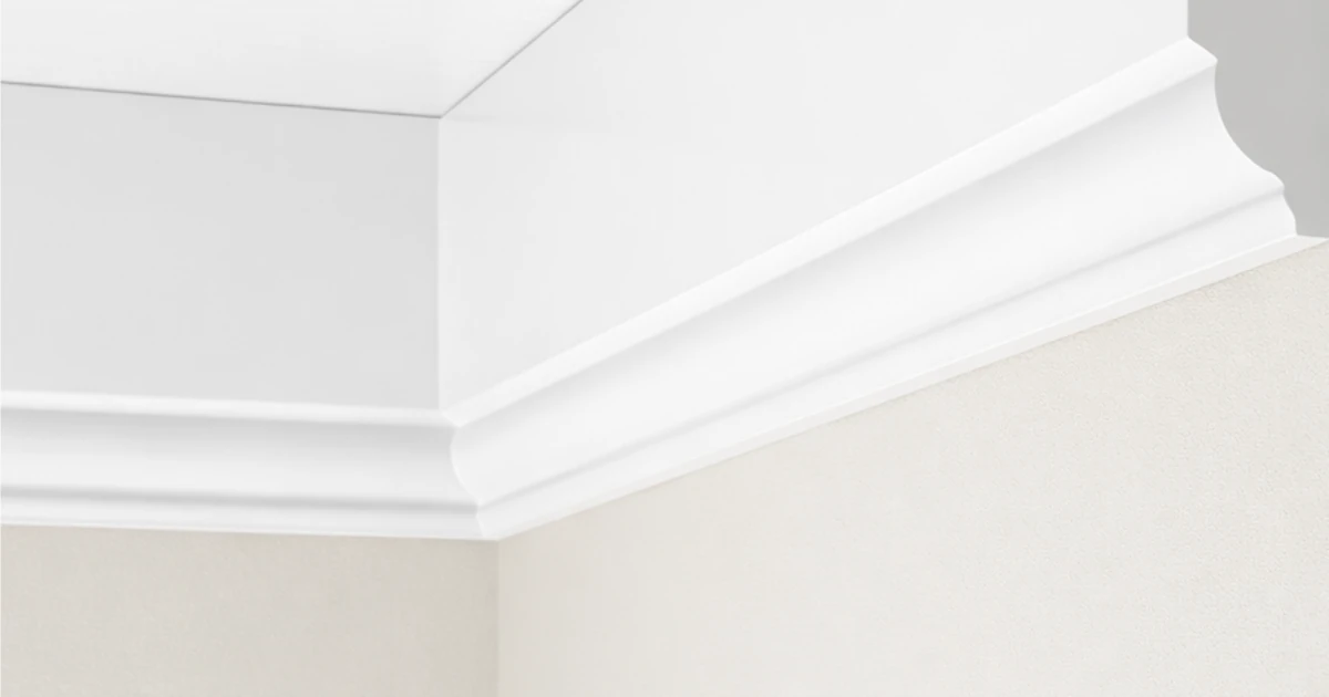Close-up of white ogee crown moulding installed at the corner of a ceiling and wall.