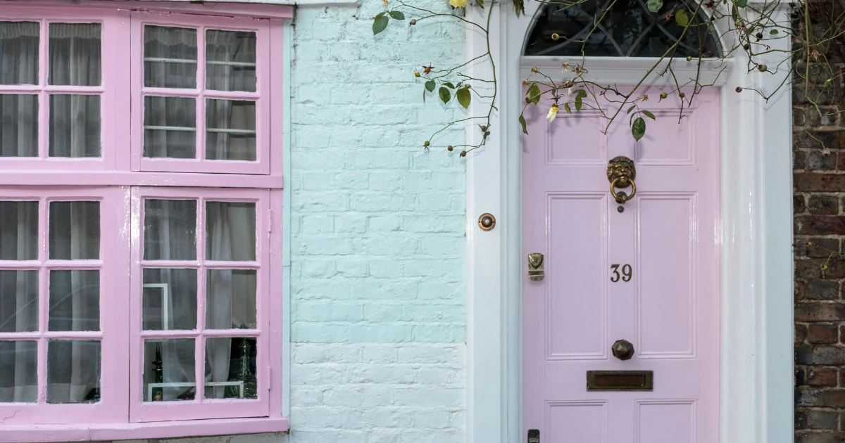 Pale pink front door numbered "39" with a brass lion knocker, matching pink window frames, and mint-painted brick on a house exterior.