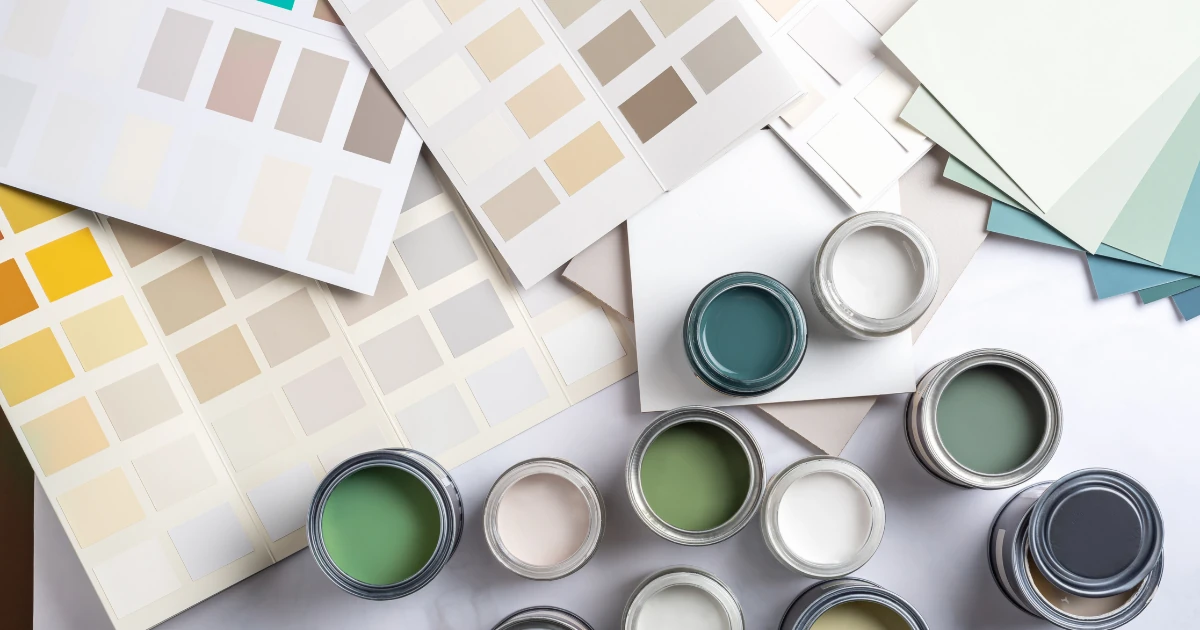 Overhead view of open paint cans in green, teal, gray, and white shades surrounded by paint color swatch cards.