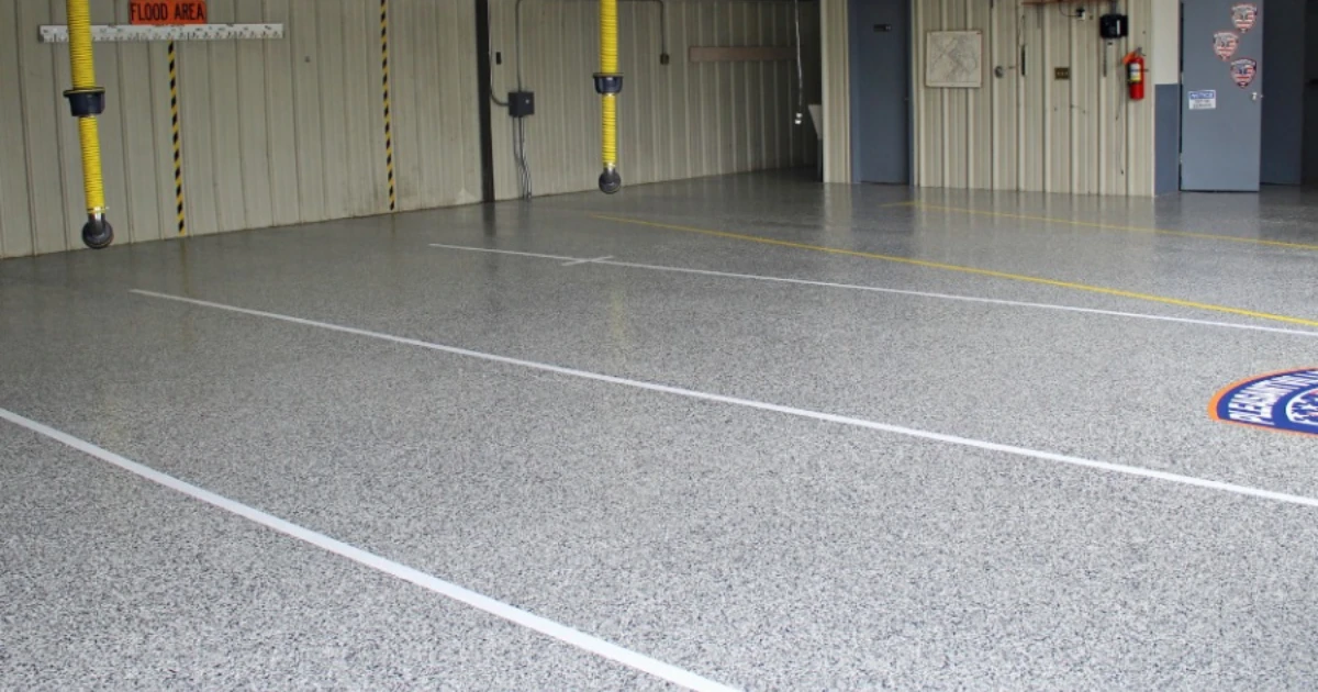 A wide view of a commercial warehouse interior with a gray speckled epoxy-coated floor, painted traffic lines, hanging yellow air hoses, and a 'FLOOD AREA' sign on the wall.