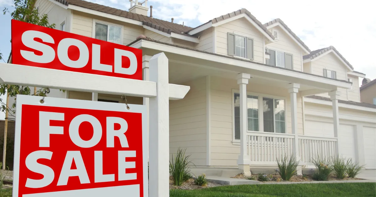Sold sign in front of a light-colored suburban home.
