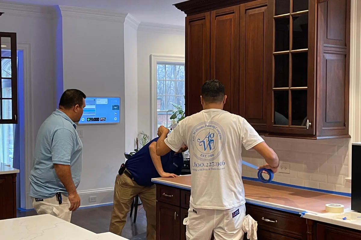 A.G. Williams painters masking countertops and backsplash before refinishing kitchen cabinets.