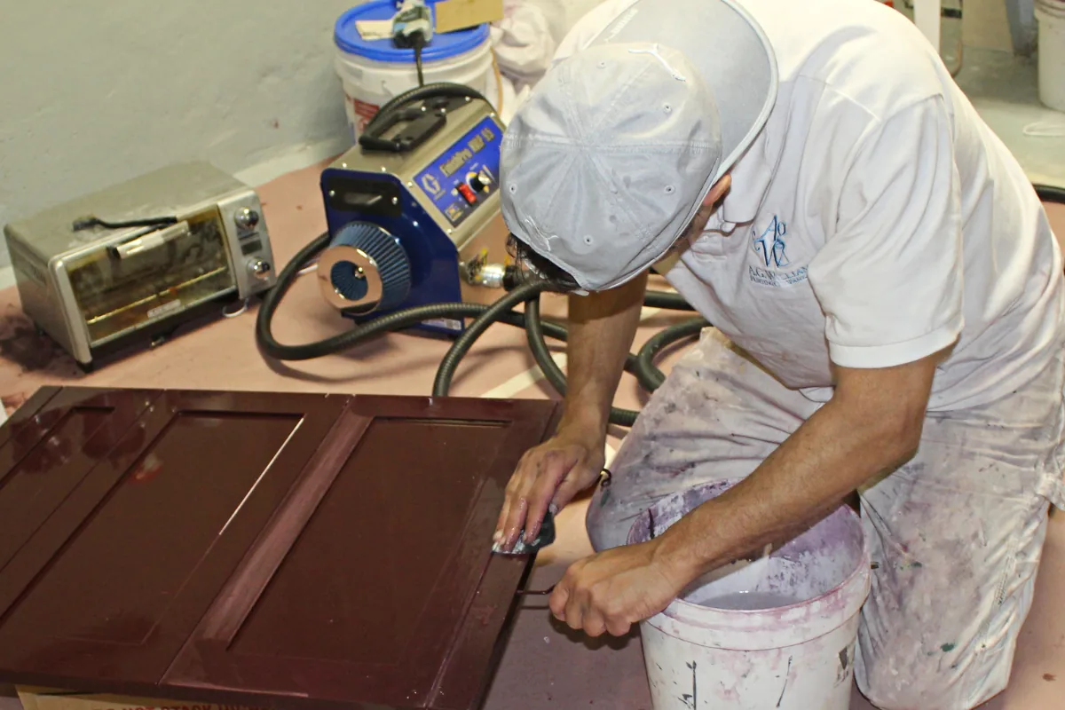 A painter degreasing and sanding a stained cabinet door before priming.