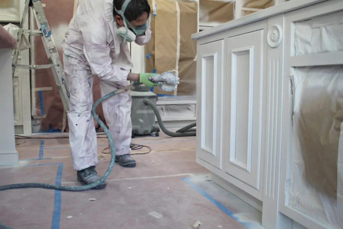 A craftsman spraying the finish coat on white kitchen cabinetry.
