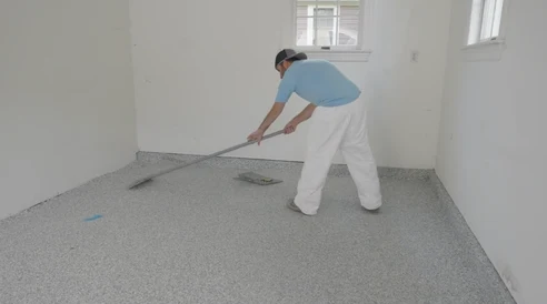 An installer scraping a cured decorative-flake floor to create an even texture.