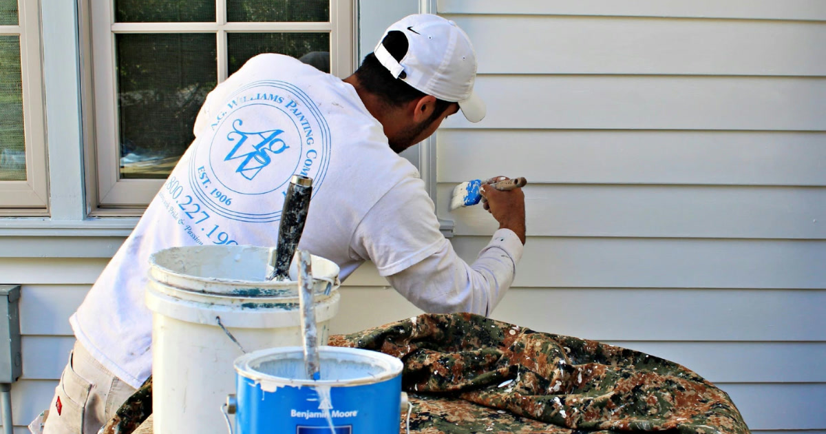 A.G. Williams painter brushing exterior trim beside a Benjamin Moore Regal Select can.