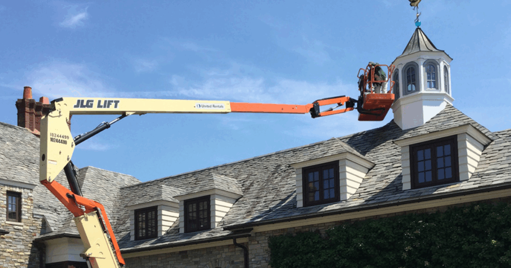 Two commercial painters using a blue scissor lift to paint the exterior of a multi-story building.
