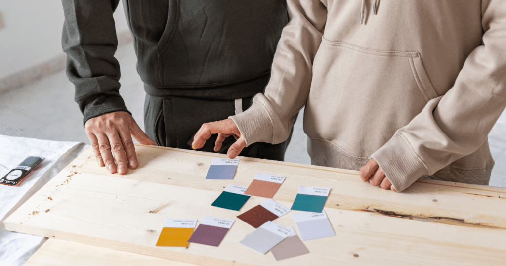 Two people examining various color swatches on a wooden board in a bright workshop.