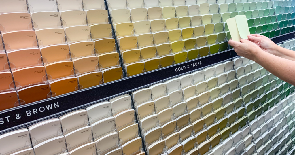 A wall with paint swatches in shades of gray, blue, and yellow, next to painting supplies and a green ladder.