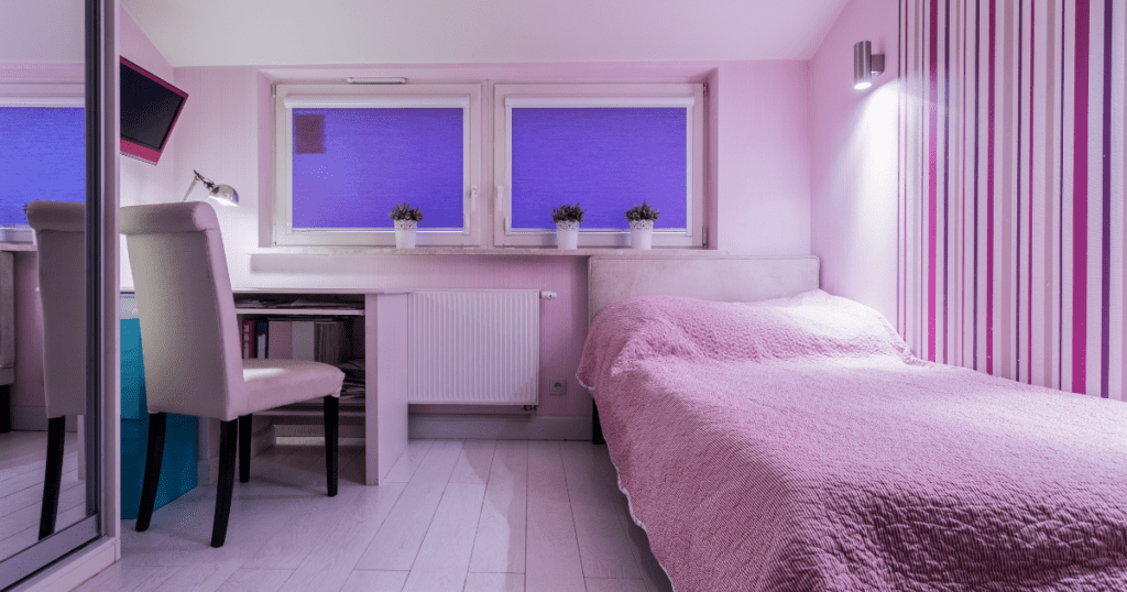 Youthful bedroom with purple bedding and walls, a small workspace, and vibrant windows.