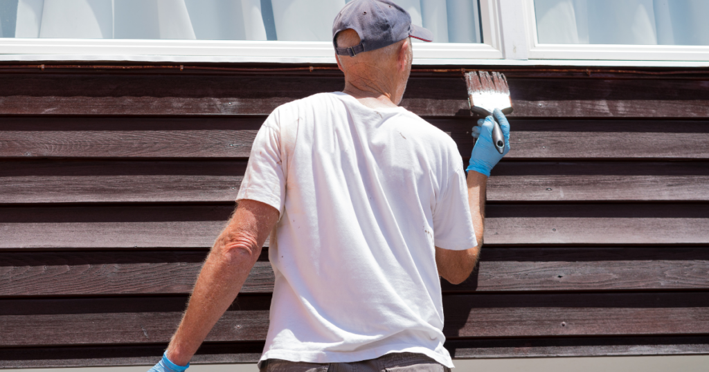 A professional painter in a white shirt and gloves carefully touching up the trim of an exterior window with white paint, ensuring a clean and precise finish.