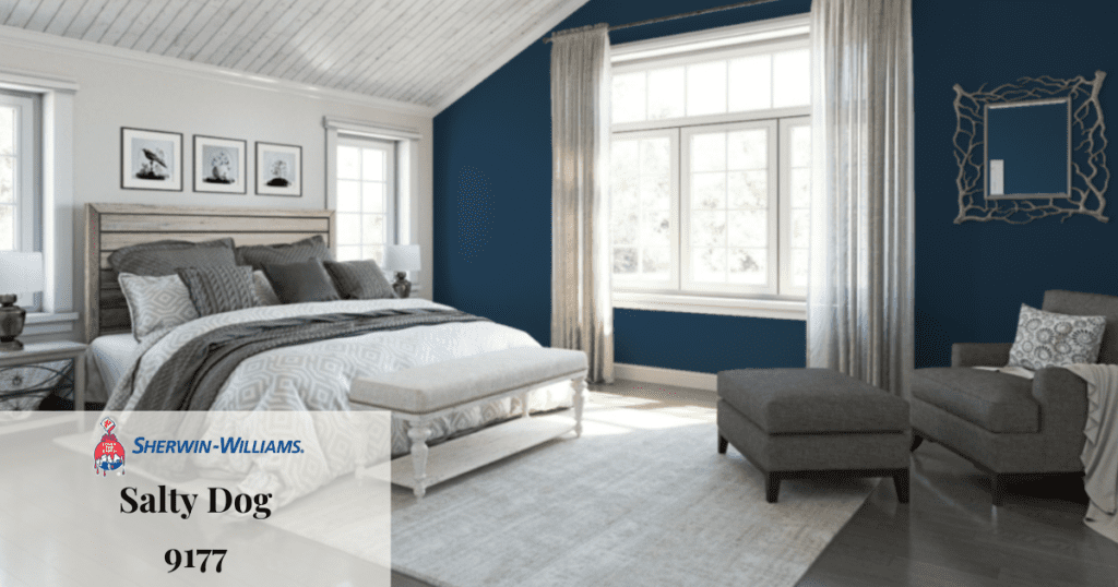 A bedroom with an accent wall painted in Sherwin-Williams' "Salty Dog" 9177, featuring gray furniture and a large window.