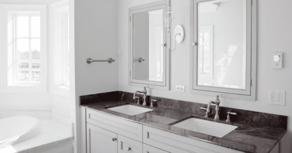 Modern bathroom with double sinks, dark stone countertops, and large windows providing natural light.