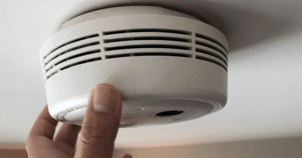 Hand testing a smoke detector on a ceiling for safety maintenance.