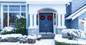 Front porch of a snow-covered home with festive wreaths on a freshly painted front door.