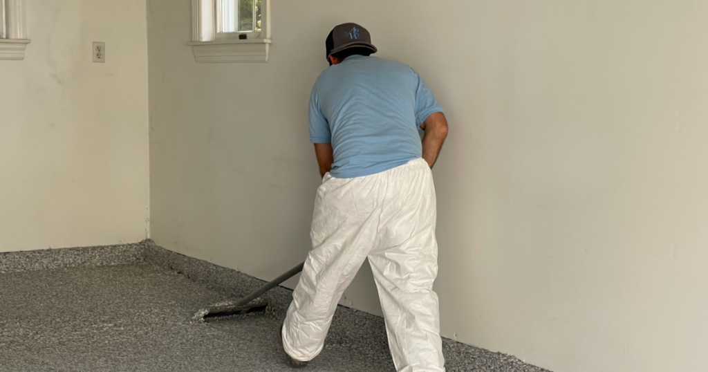 A professional technician applying a polyurea floor coating to a garage, focusing on precision for a seamless, durable finish.