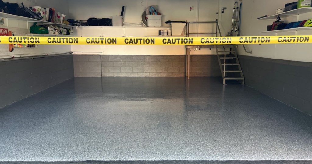 A completed garage floor with a high-gloss polyurea coating, roped off with caution tape to protect the curing process.