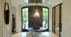 A bright and modern entryway featuring a black arched double door with glass panes, a circular table with decorative pinecones, and natural light illuminating the hardwood floors.