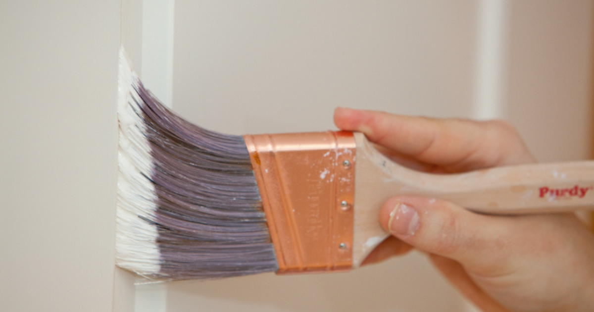 A close-up of a hand painting a white trim with a high-quality angled paintbrush, showcasing careful attention to detail.