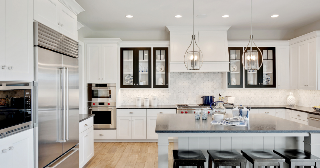 A bright and modern kitchen featuring white cabinetry paired with glass cabinetry that has black trim, black countertops, and pendant lighting over a central island with stools.