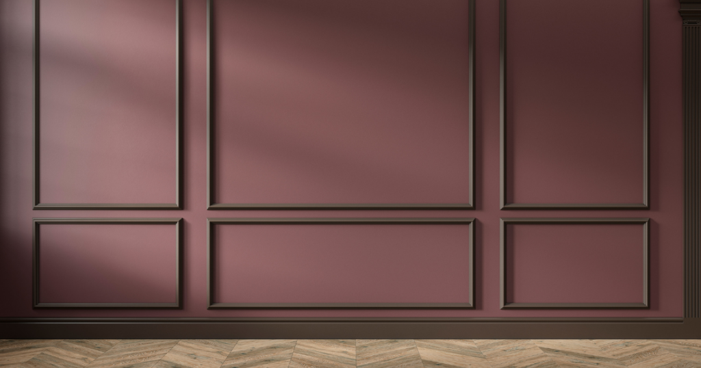 A sophisticated burgundy accent wall with decorative panel molding and rich wood flooring.