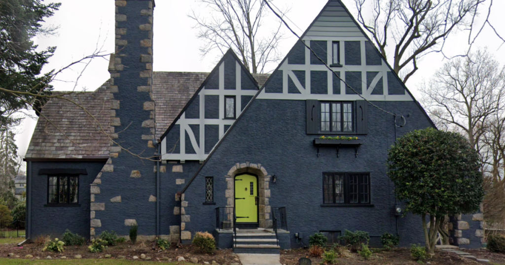 A Tudor-style home with a dark gray exterior, white trim, and a bold green front door.