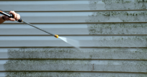 A pressure washer effectively removing dirt and green mold from vinyl siding through pressure washing, revealing a clean surface.