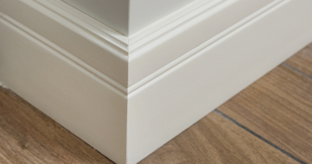 Close-up of a white baseboard with smooth edges and a seamless finish, meeting natural wood flooring.