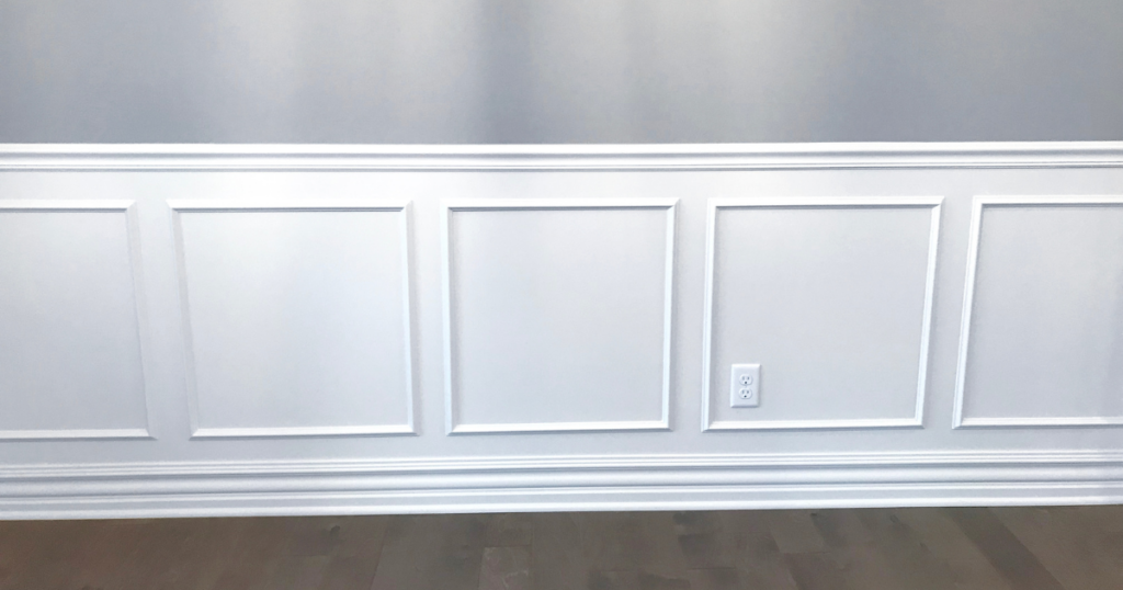 A section of custom white wainscoting with crisp, clean lines and a professional finish against a light gray wall.