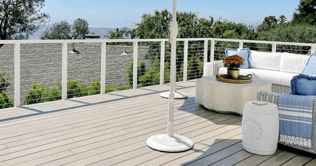 A clean, light-stained deck with white railing, modern furniture, and scenic hillside views.