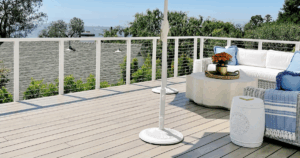 A clean, light-stained deck with white railing, modern furniture, and scenic hillside views.